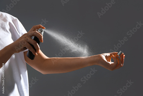 Young woman spraying elegant perfume on grey background, closeup photo