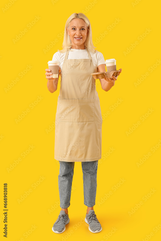 Mature woman with cups of coffee on yellow background Mature woman with cups of coffee on yellow background