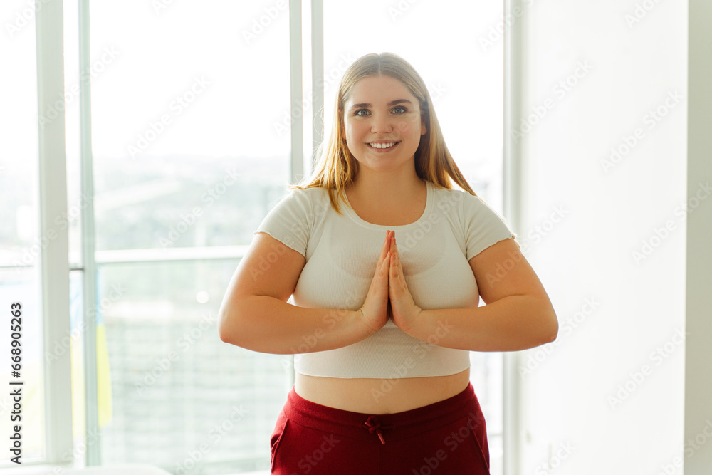 Smiling young woman standing standing on mat yoga looking at camera at home in apartment