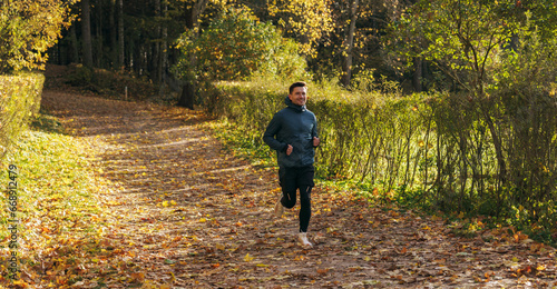 Jogging, warm-up every day, healthy lifestyle. Man training in the afternoon in the autumn cold season in the park. The athlete is wearing warm sports clothes and fitness sneakers.