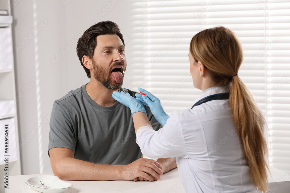 Fototapeta premium Doctor taking throat swab sample from man`s oral cavity indoors