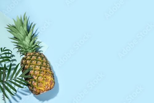 Whole ripe pineapple and green leaves on light blue background  flat lay. Space for text