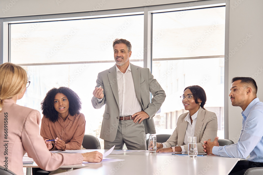 Busy international executive company team with older leader discussing work plan at board meeting. Diverse employees and ceo managing consulting communicating in boardroom corporate office.