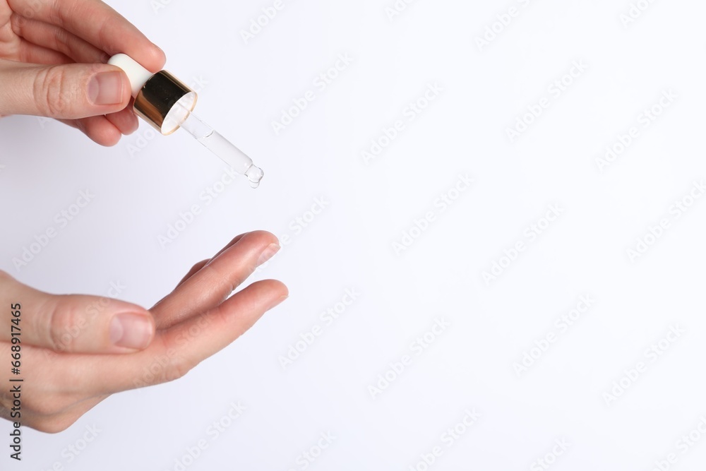 Woman applying cosmetic serum onto fingers on white background, closeup. Space for text Woman applying cosmetic serum onto fingers on white background, closeup. Space for text