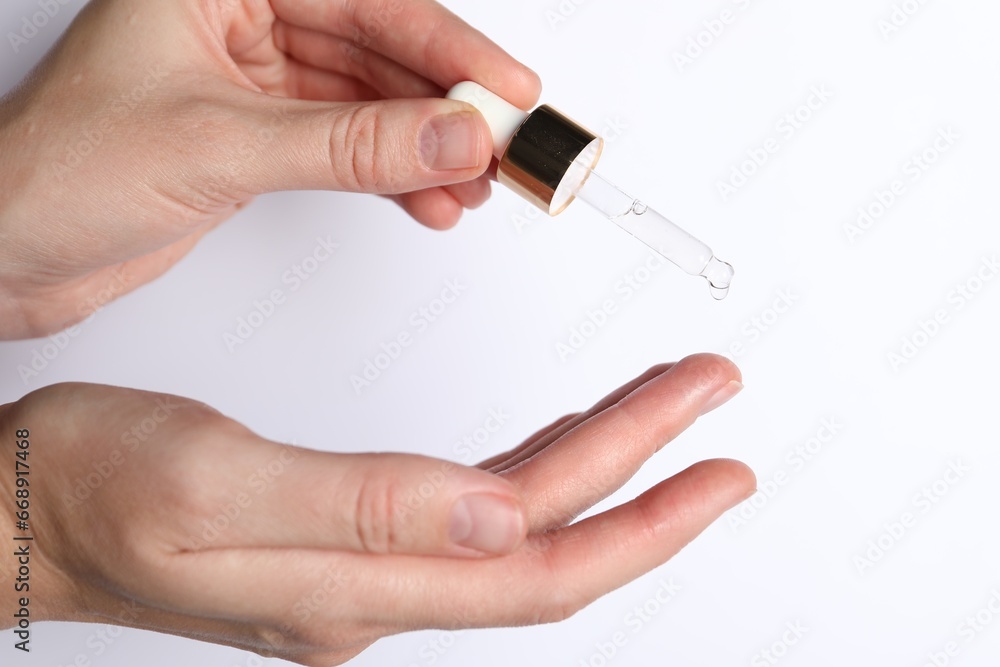 Woman applying cosmetic serum onto fingers on white background, closeup