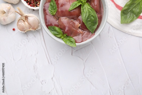 Bowl with raw chicken liver, garlic, peppercorns and basil on white textured table, flat lay. Space for text