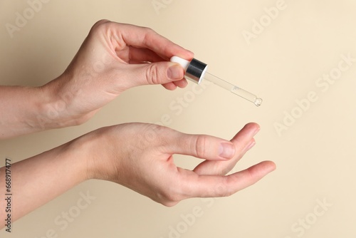 Woman applying cosmetic serum onto finger on beige background  closeup
