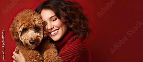 Smiling woman lovingly embraces her brown Spanish water dog against a red background representing love for animals photo