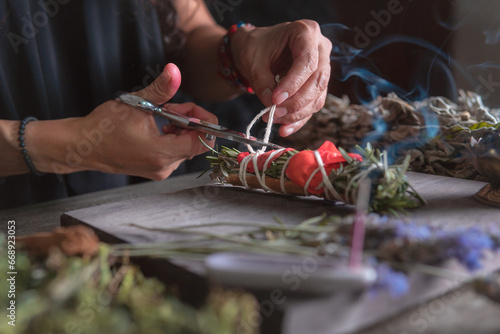 woman doing traditional ritual with herbs tying them with cotton thread accompanied by incense