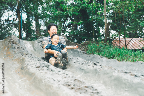 Asian happy mother and child have activities together on holidays. Mom and her son playing slider that made from mud. Happy harmonious family outdoors and learning concept.
