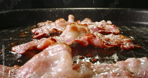 Frying pork bacon in pan side view close up slow motion. Splashes of sizzling oil. Pan-fried bacon slices capture the essence of sizzling goodness, ready to be devoured with delight. Fried to perfect