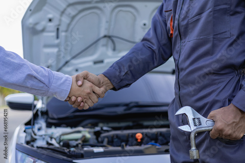 At Auto Service. Cropped view of auto mechanic and customer holding hands, car repair, maintenance, people gesture and concept, mechanic with clipboard and man or owner shaking hands at car shop