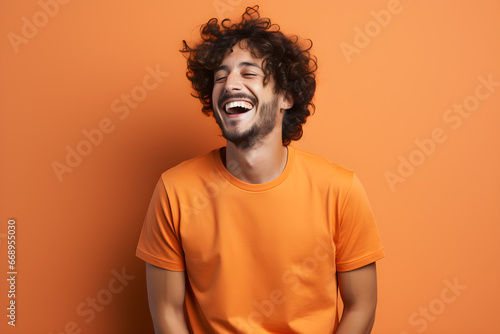 Young man, donned in an orange t-shirt, exuberantly laughs against an isolated orange backdrop © oshadax