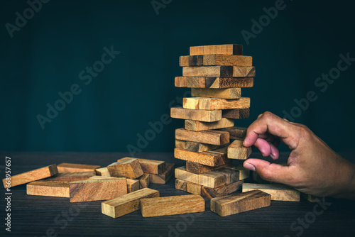 Hand pull wooden block tower stack in pyramid stair step with caution to prevent collapse or crash concepts of financial risk management and strategic planning and business challenge plan.