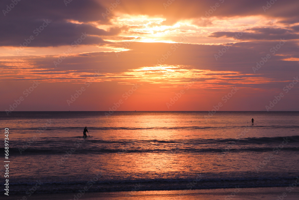 Silhouettes of surfers on a SUP board in the sea against the backdrop of a colorful sunset. Tropical island, vacation, active recreation at sea, travel.