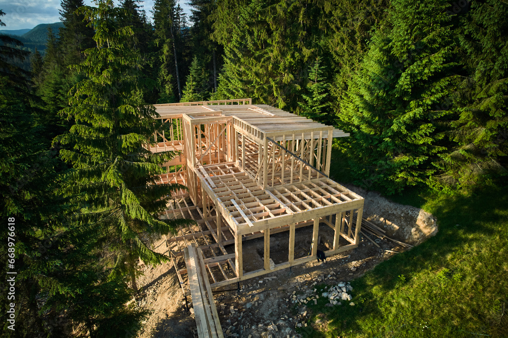 Drone view of two-story wooden frame house under construction near forest. Idea of modern ecological construction and contemporary architectural design. Drone view of two-story wooden frame house under construction near forest. Idea of modern ecological construction and contemporary architectural design.