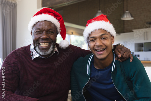 Happy african american father and son in christmas hats having video call, smiling