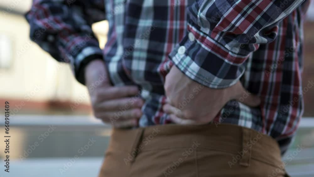 A man feels a sharp pain in his lower back and massages his back during a break at work. Sports and injury concept. A man feels a sharp pain in his lower back and massages his back during a break at work. Sports and injury concept.