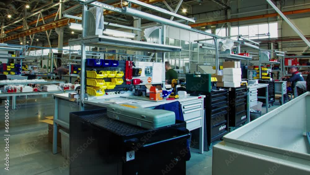 Employees work at tables assembling devices from details taken from boxes on shop floor. Staff members use special equipment in process time lapse Employees work at tables assembling devices from details taken from boxes on shop floor. Staff members use special equipment in process time lapse