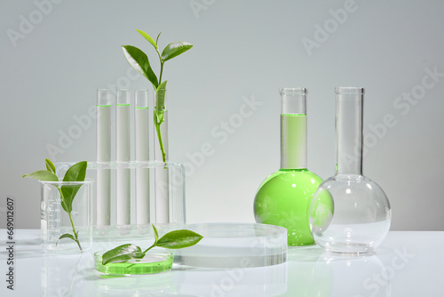 On a white background, some green tea leaves, a few test tubes containing clear liquid, a beaker holding green liquid extracted from green tea. Mockup for pharmaceutical or cosmetic advertising.