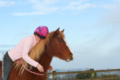 Love is, pretty young woman and her pretty chestnut pony horse share an emotional moment as she sits on the horses back  hugging it whilst outdoors in field. photo