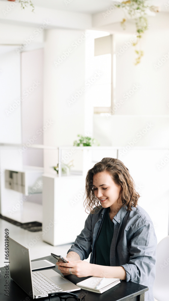 Young Woman Embracing the Modern Work Environment: Using Laptop Computer and Mobile Phone at Office. Student Girl Engaged in Productive Work from Home. Freelancing, Business, E-Learning Young Woman Embracing the Modern Work Environment: Using Laptop Computer and Mobile Phone at Office. Student Girl Engaged in Productive Work from Home. Freelancing, Business, E-Learning