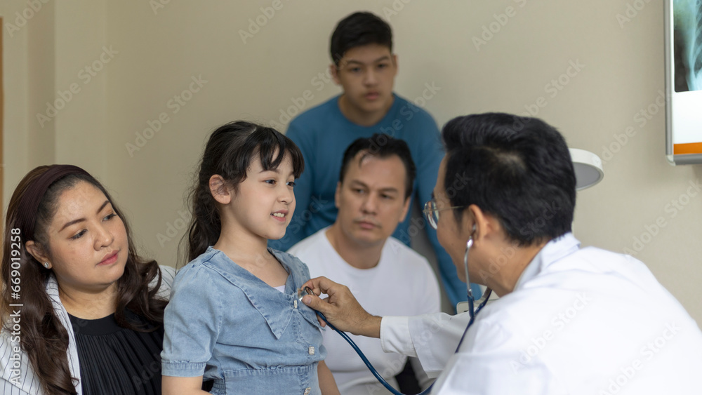 Fototapeta premium Doctor uses stethoscope to check a girl's lung in his clinic. Doctor discusses with a girl's family for a medical treatment program.