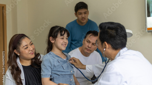 Doctor uses stethoscope to check a girl's lung in his clinic. Doctor discusses with a girl's family for a medical treatment program.