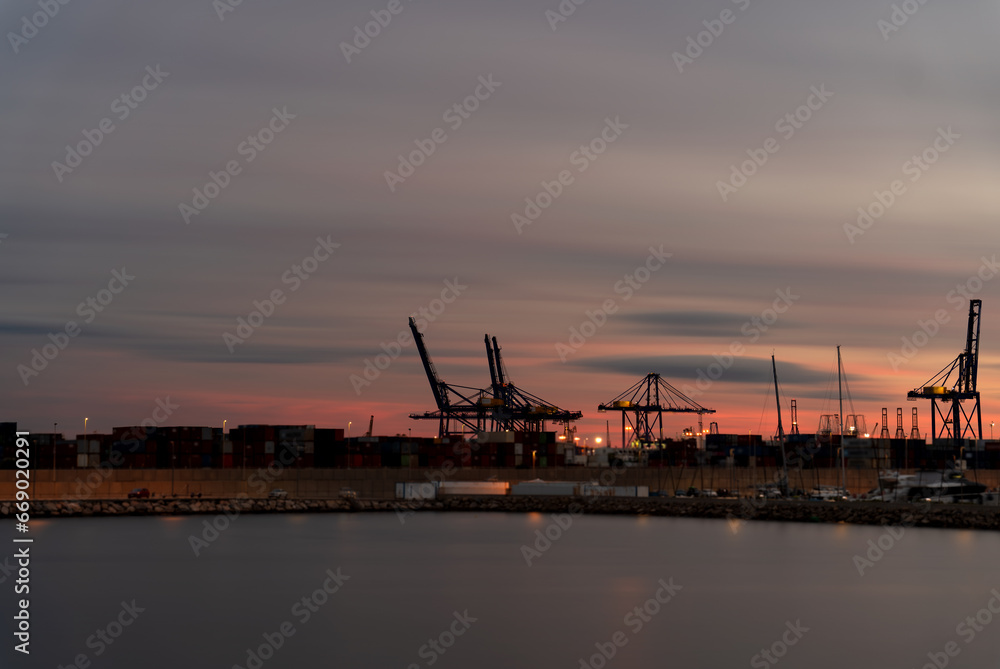Dusk at the bustling commercial port with silhouette of giant cranes