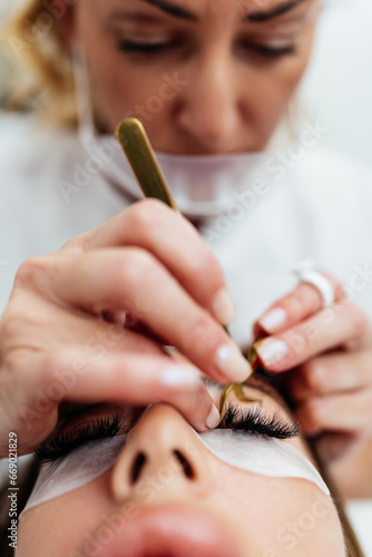 Beautiful young adult woman receiving professional eyelash makeup treatment. Cosmetician is smiling and looking at camera. Beauty and cosmetics business.