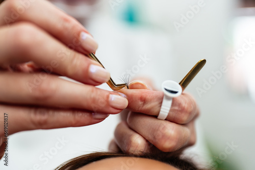 Beautiful young adult woman receiving professional eyelash makeup treatment. Cosmetician is smiling and looking at camera. Beauty and cosmetics business.