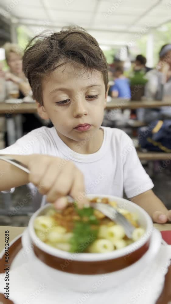 Young Boy Struggles to Eat Italian Pasta, Receiving Assistance from His Mother During Lunch at a Restaurant Young Boy Struggles to Eat Italian Pasta, Receiving Assistance from His Mother During Lunch at a Restaurant