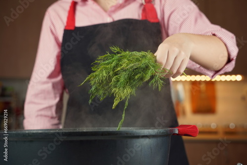 Woman adding fresh dill at chicken soup, chicken broth, in a pot. Healthy food concept