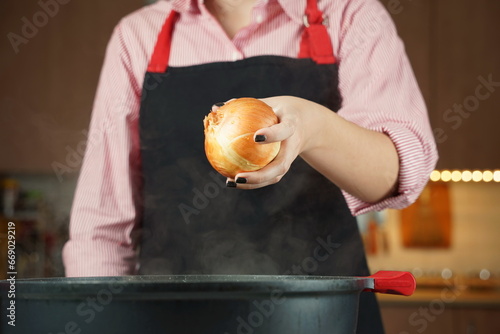 Woman adding onion with skins at chicken soup, chicken broth, in a pot. Healthy food concept