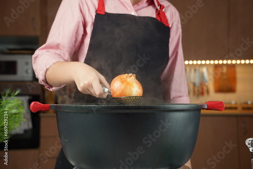 Woman adding onion with skins at chicken soup, chicken broth, in a pot.. Healthy food concept