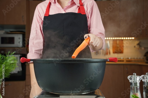 Woman adding fresh carrot at chicken soup, chicken broth, in a pot. Healthy food concept