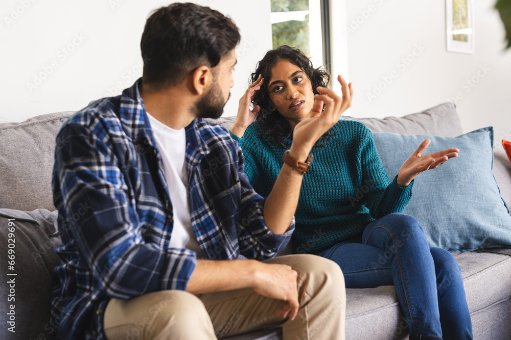 Angry biracial couple sitting on sofa and arguing in living room at home Angry biracial couple sitting on sofa and arguing in living room at home