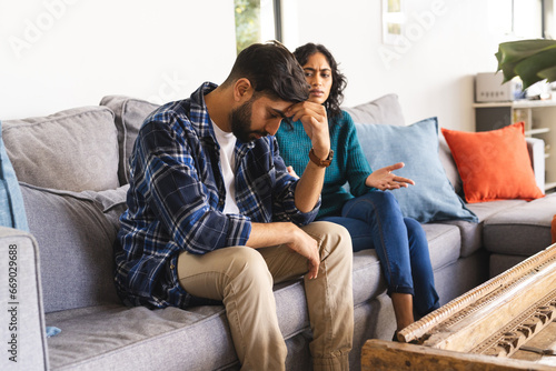 Angry biracial couple sitting on sofa and arguing in living room at home photo