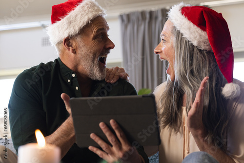 Happy senior caucasian couple sitting on sofa using tablet for christmas video call at home photo