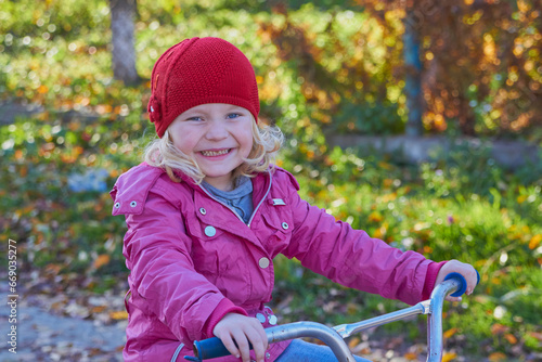 little girl laughs on a bicycle in autumn,a sincere smile of a child sitting on a bicycle, a happy childhood, a child in autumn