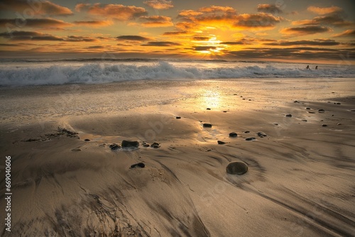 a sunset over the ocean at an empty beach with waves and stones