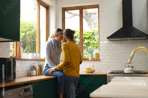 Happy, romantic caucasian couple embracing sitting on worktop and standing in kitchen, copy space photo