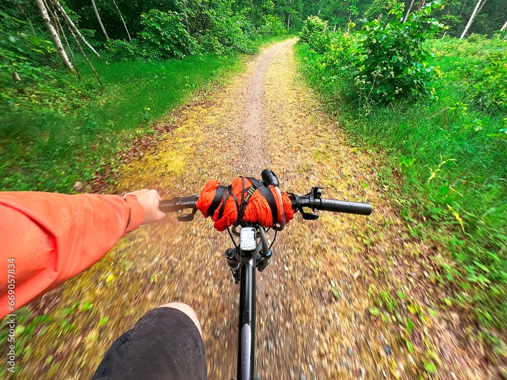 Naklejka premium First-person view of handling the bicycle on the forest road in the city towards sunlight. Concept of using a bicycle for sports and recreation out of a town.