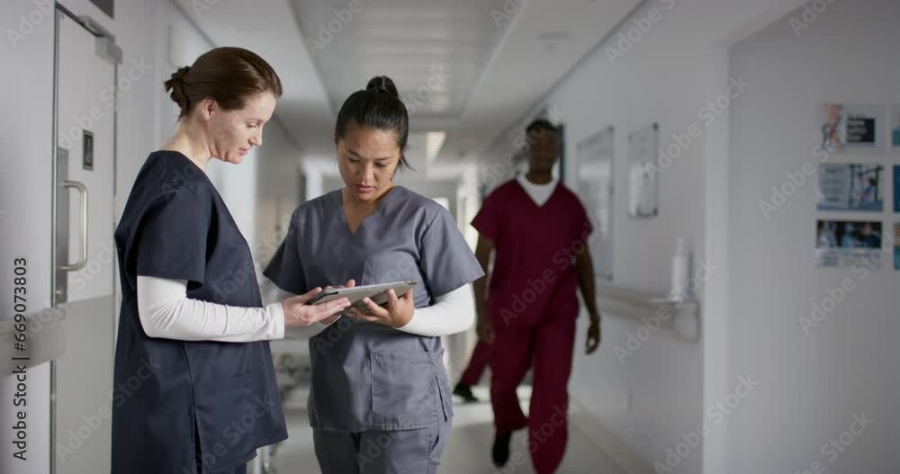 Diverse female doctors discussing work, using tablet in corridor at hospital, slow motion Diverse female doctors discussing work, using tablet in corridor at hospital, slow motion