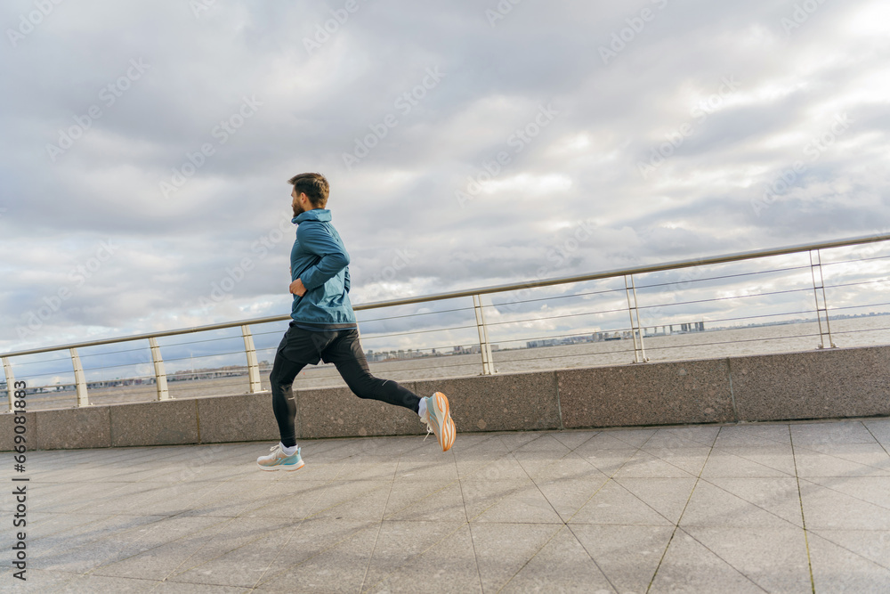 A slender, hardy man runs alone training in the cold. Athlete jogging in warm sportswear for autumn.  Fitness trainer active lifestyle for health.