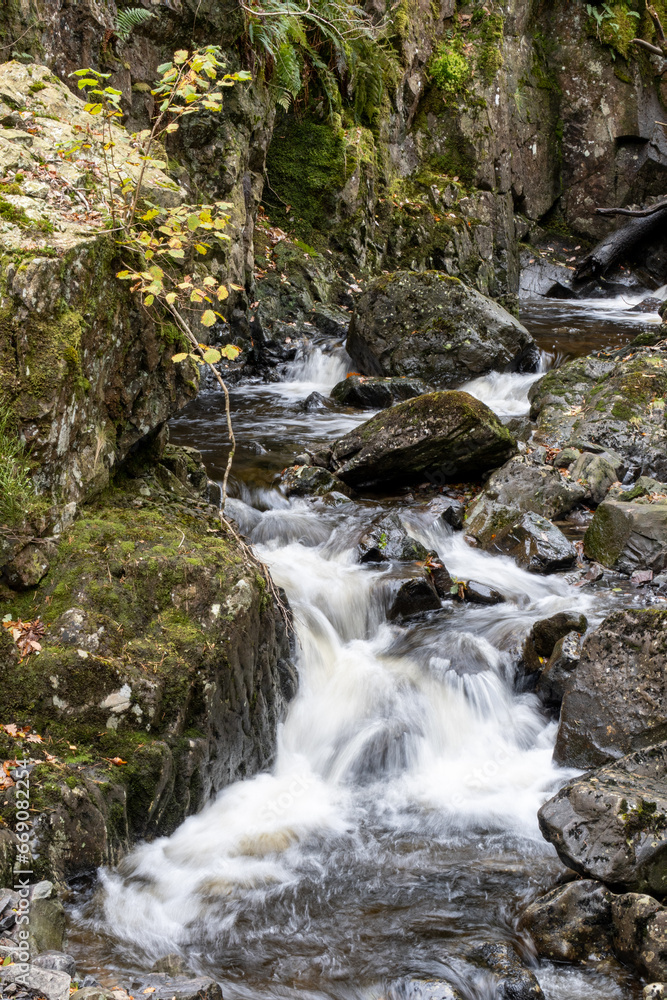 Fast flowing water falls amid rocks and woodland