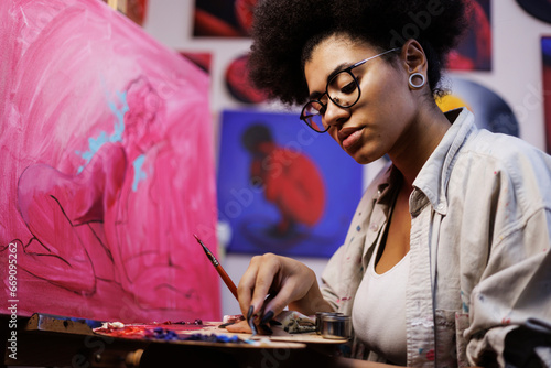 Fotografie Focused african american artist mixing colors on palette near canvas on easel in