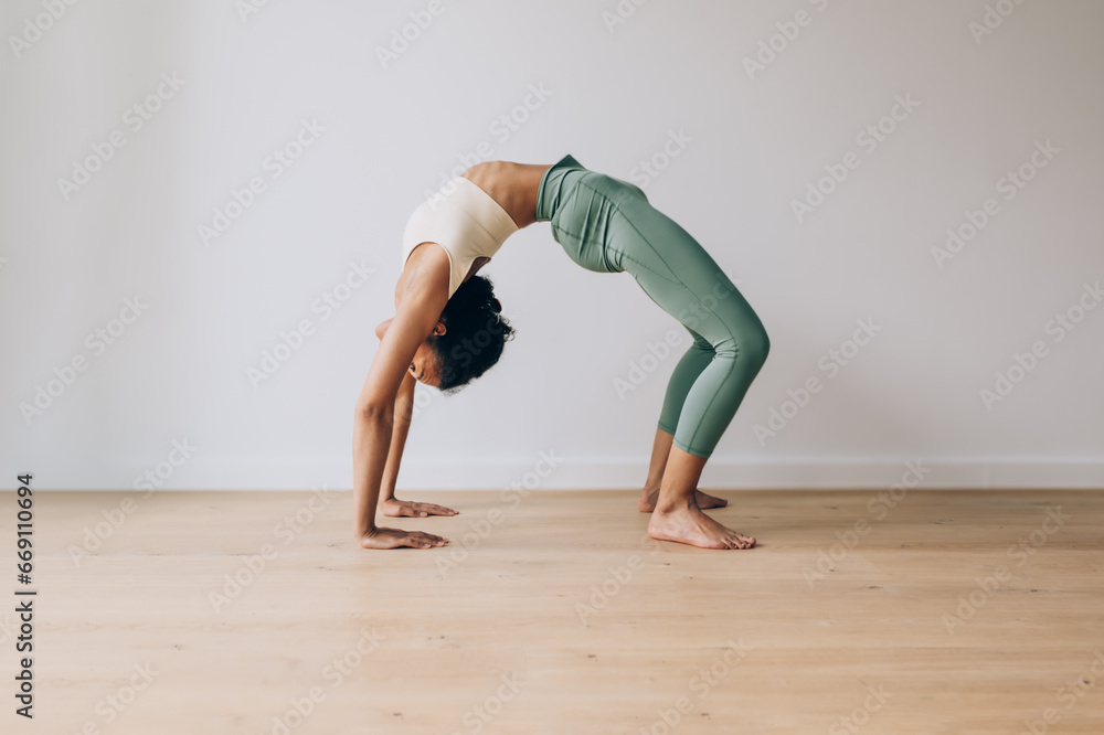 yoga teacher practicing yoga position of bridge against white wall and wood floor with copy space