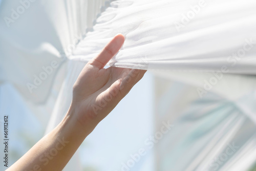 Woman hand holding white clean fabric curtain drape or clothes outdoor gently after use sunlight dry fabric after laundry. Concept of housewife washing clothes in weekend lifestyle. photo
