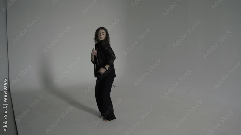 Beautiful curly woman in black clothes slowly dances barefoot on a cyclorama in a white photo studio Beautiful curly woman in black clothes slowly dances barefoot on a cyclorama in a white photo studio
